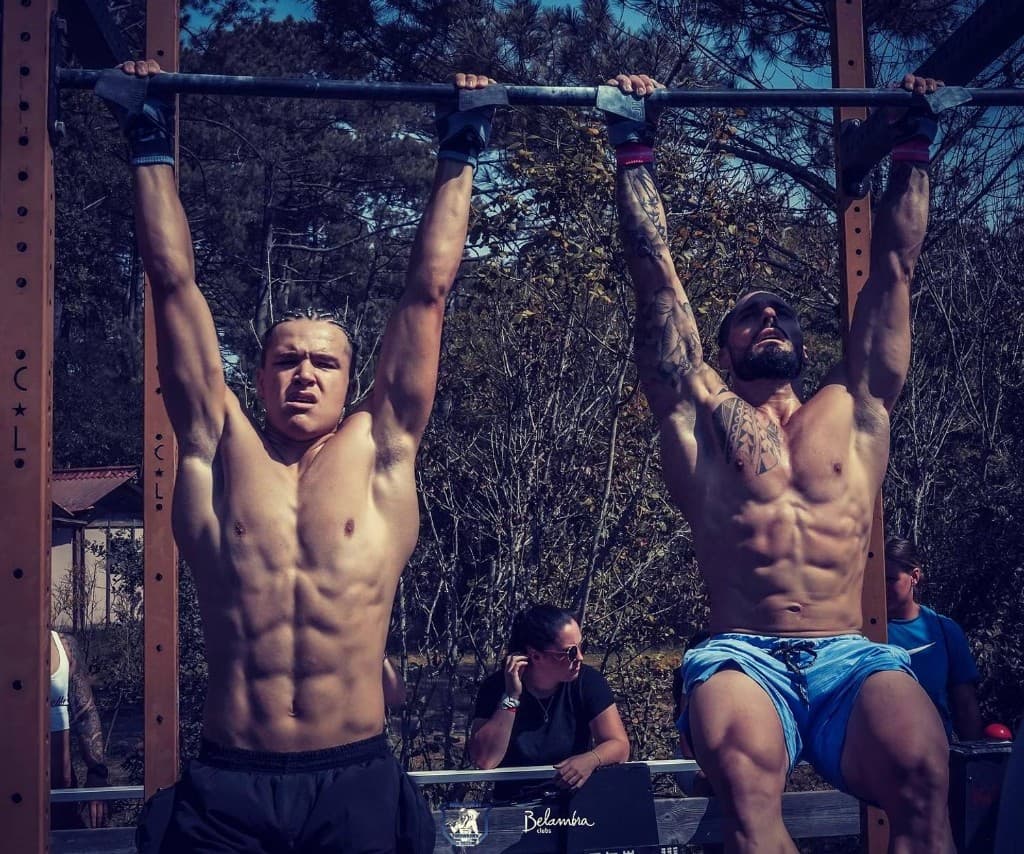 Deux athlètes en suspension à la barre de traction, entraînement en extérieur — Belambra